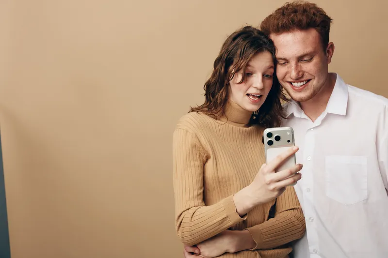 Young couple looking at smartphone screen with surprised and happy expressions. Casual clothing and neutral background. Concept of technology, communication, and relationship moments.