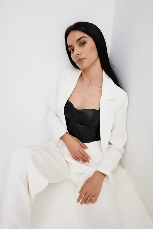 young woman posing confidently in white suit and black top against minimalist white background with long dark hair and natural makeup, stylish and modern look