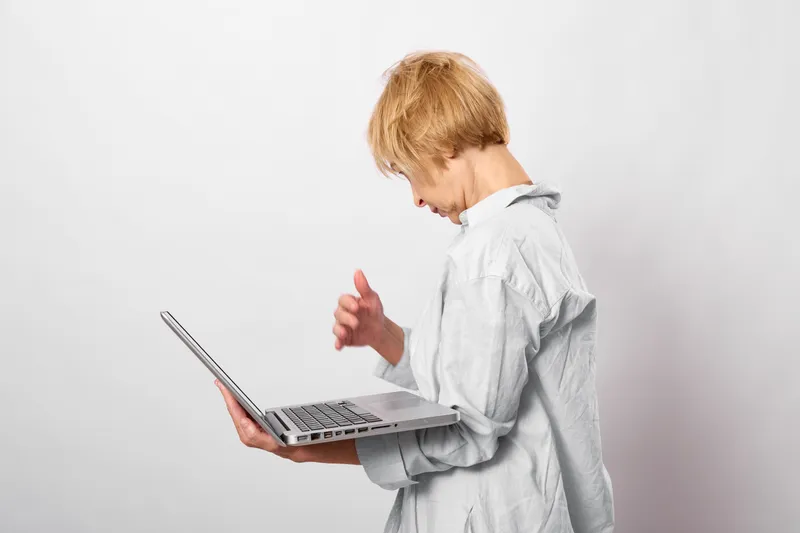Child with blond hair uses a laptop on a white background, focused on the keyboard and screen, learning through technology and education for online study
