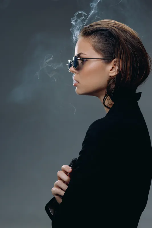 Profile of a serious woman with sunglasses and short hair smoking against dark background