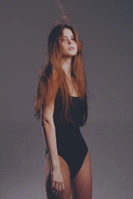 Young woman posing in black swimsuit with long hair against gray background, fashion portrait, elegance, style
