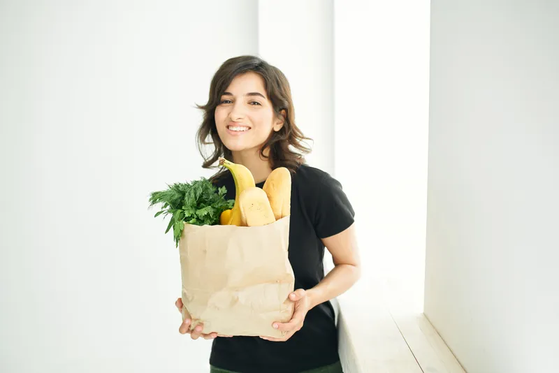 Весёлая брюнетка с продуктовым пакетом готовит здоровую пищу