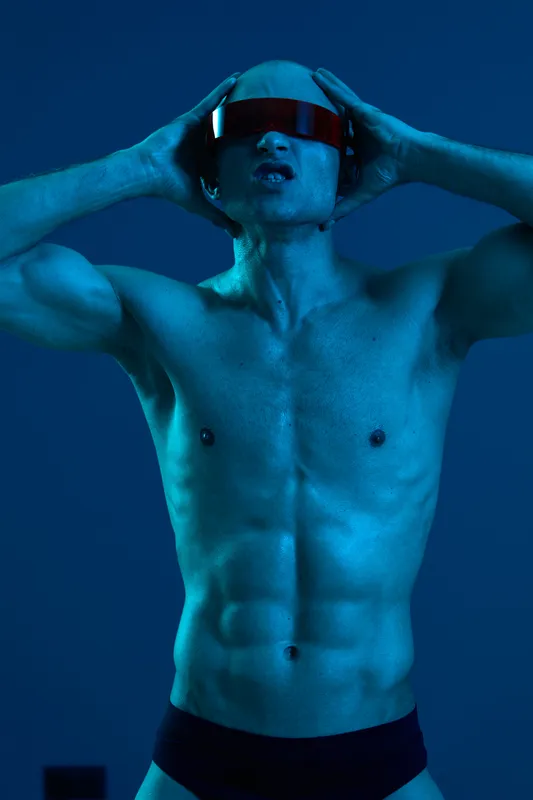 Strong man wearing futuristic glasses poses dramatically against a blue backdrop, capturing an energetic and modern aesthetic. The image exudes a sense of power and style.