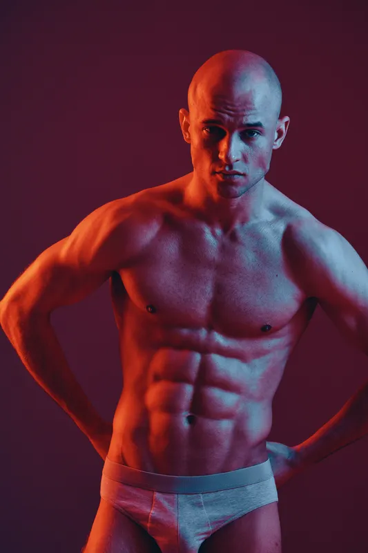 Athletic man posing confidently against a vivid background, showcasing a fit physique with dramatic lighting effects. A captivating blend of strength and artistry.