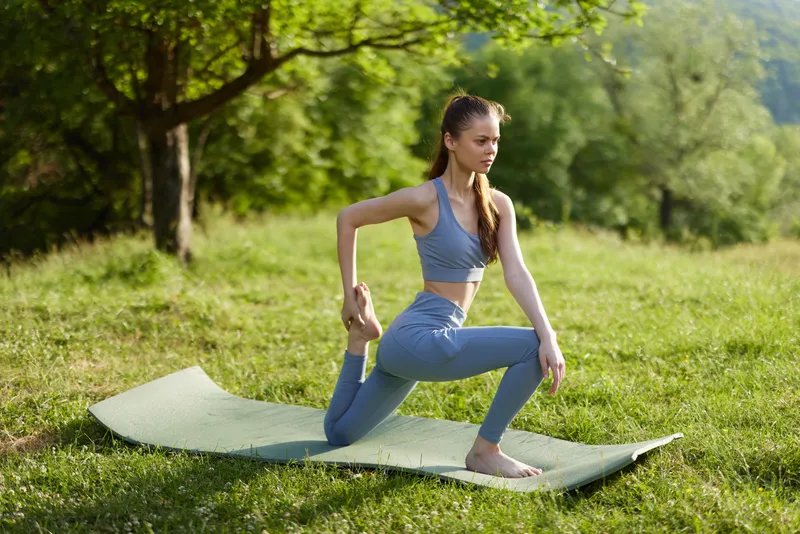Fit young woman practicing yoga outdoors in a serene green setting, showcasing flexibility and peace of mind during a sunny day in nature