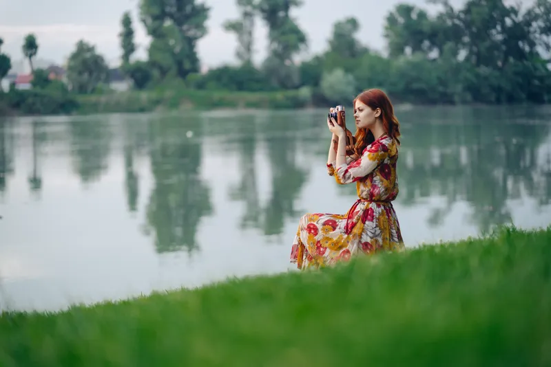 Женщина в платье с фотоаппаратом на природе делает снимки, хобби