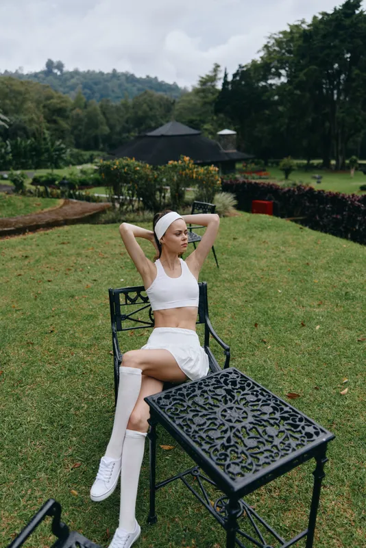 Young woman in sporty attire relaxing outdoors, showcasing active lifestyle and wellness, surrounded by nature, summer vibes, stylish and energetic atmosphere
