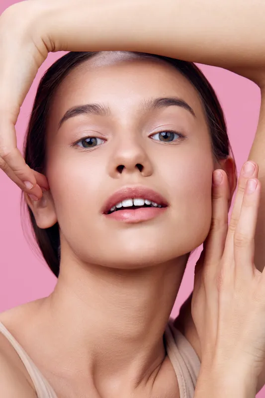 Close up portrait of a young woman with natural makeup, showcasing healthy skin and glowing beauty against a soft pink background, embodying confidence and self care