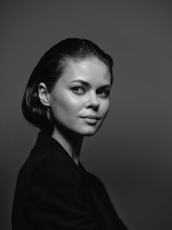 Black and white portrait of a young woman with short hair and confident expression wearing a dark outfit in studio lighting.