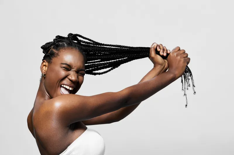 Energetic young woman with braided hair, joyfully expressing herself against a minimalistic background, showcasing confidence and vibrancy