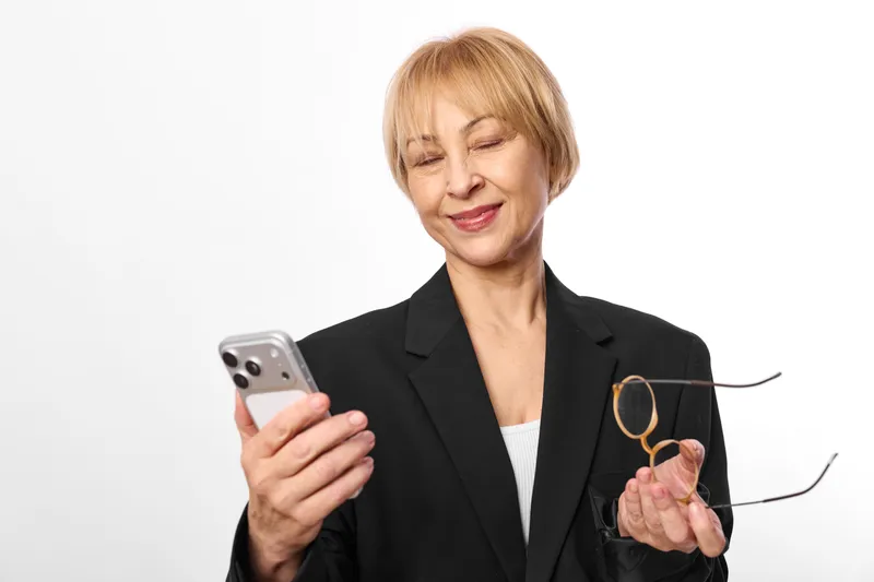 Woman with smartphone and glasses, smiling in a studio portrait, business jacket on white background, conveying communication and technology, friendly mood
