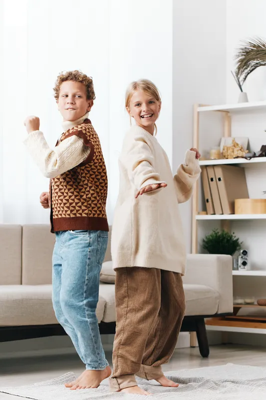 Authentic lifestyle scene featuring two children dancing in a cozy living room, highlighting school readiness, creativity, and spontaneous playful movement.