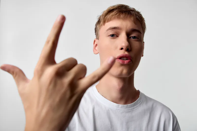 Hand gesture, rock on, young man, white t shirt, facial expression, confidence, attitude, lifestyle. Close up scene highlighting bold pose and intense gaze suitable for music, youth culture and