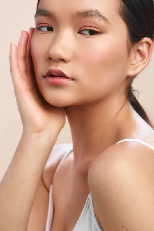 asian woman gazes softly to the side, close up portrait with hand near cheek, soft lighting, clear skin, calm mood, minimal backdrop, subtle elegance and natural beauty.