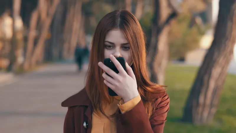 Симпатичная женщина в пальто с телефоном в руке гуляет в парке, отдыхает