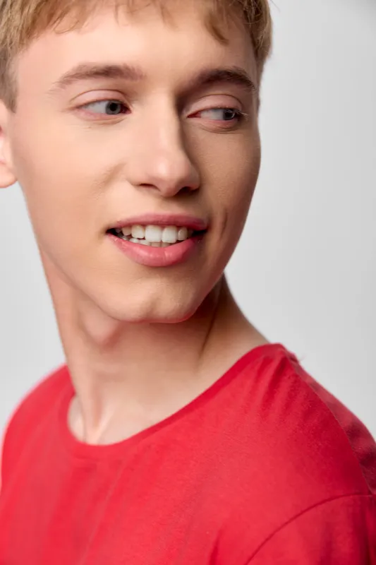 Young man in a red shirt turns his head with a light smile, casual studio mood, clean background, soft lighting, contemporary fashion