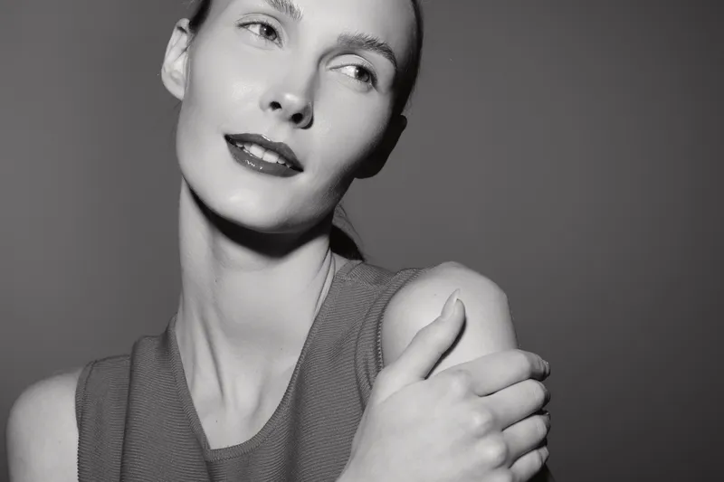 Portrait of a young Caucasian woman with fair skin posing with crossed arms, looking away thoughtfully. Concept of natural beauty, elegance, and minimalism in monochrome photography.
