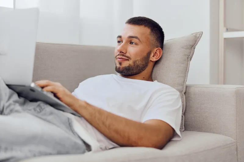 Relaxed man working on a laptop at home, experiencing the blend of work and personal life, while embracing authentic imperfection and solo living choices.