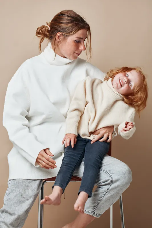Мать и дочь проводят время вместе в уютных белых свитерах, сидя на стуле