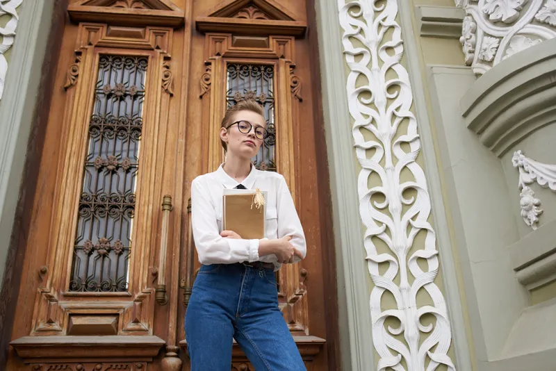 Коротко стриженная женщина с книгой в руках читает на открытом воздухе