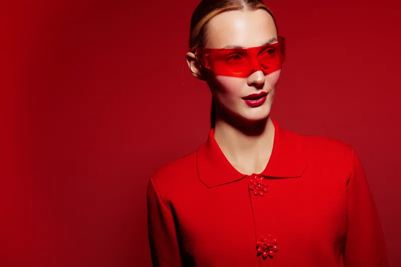 Stylish woman in red outfit and red sunglasses poses on red background. Fashion portrait with bold color contrast and modern accessories. Concept of style and confidence.
