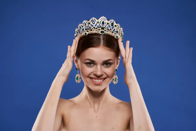 Красивая женщина с обнажёнными плечами, украшениями и косметикой, привлекательный взгляд на голубом фоне