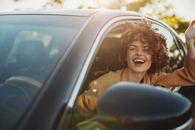 A joyful woman in a car with window down, hair in the breeze, bathed in warm retro tones. A candid lifestyle moment that conveys joy, travel, and sunny freedom. Perfect for lifestyle and travel