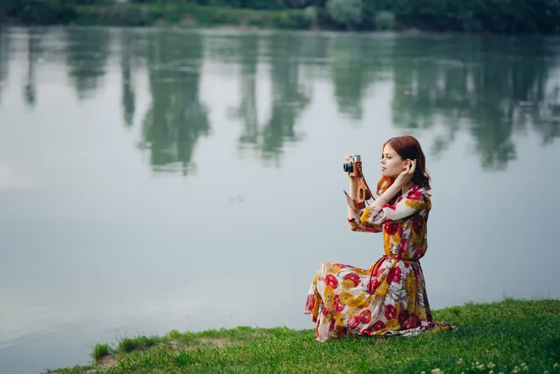 Женщина в платье с фотоаппаратом на природе, занимающаяся своим хобби — фотографией