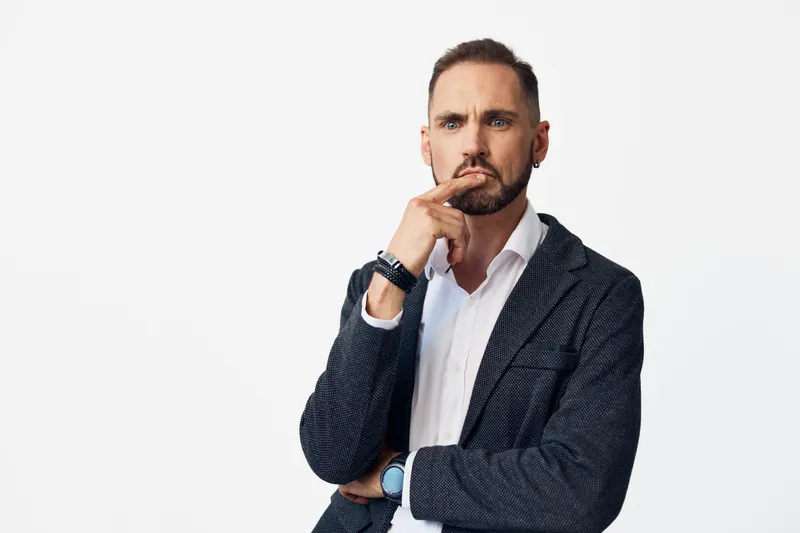 A professional man stands against an isolated colored background, projecting business confidence as he ponders a solution, showcasing thoughtful focus and calm, controlled emotion.