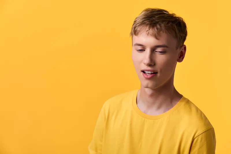 Young man in a yellow tshirt against a matching yellow studio background, relaxed pose and soft expression, vibrant color mood for fashion or lifestyle use