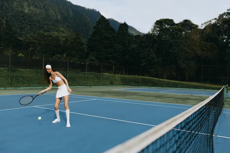 Young female tennis player in stylish sportswear on a blue tennis court, demonstrating focus and determination while preparing to serve