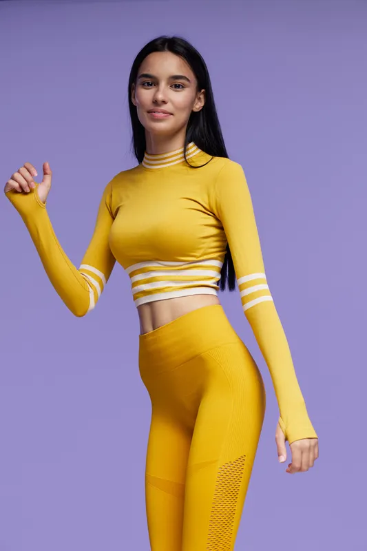 Young woman sport fitness wearing yellow athletic outfit posing confidently on purple background, showing healthy lifestyle and active energy in studio setting.