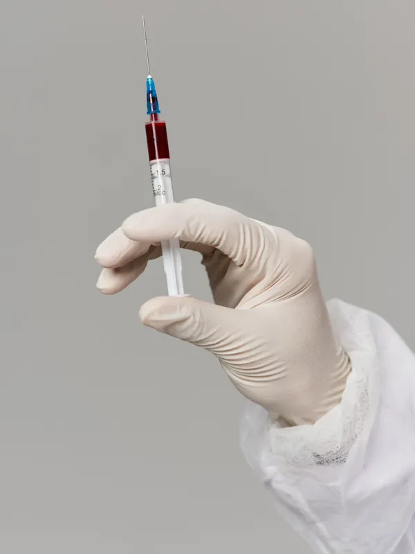 Рука в медицинской перчатке держит шприц с вакциной от COVID-19 в исследовательской лаборатории