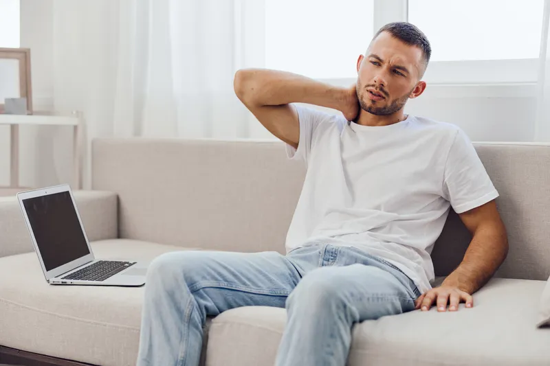Man experiencing discomfort while working on a laptop at home, showcasing modern home office vibes. Ideal for wellness and productivity themes.