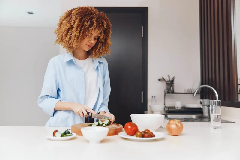 Привлекательная афроамериканка готовит вкусное блюдо в уютной домашней кухне, делая акцент на здоровом образе жизни
