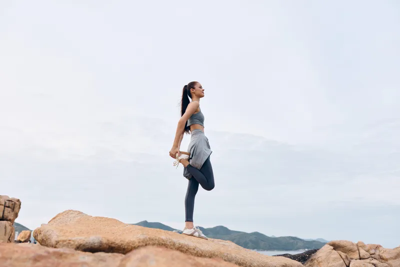 Young model practicing yoga on rocks in nature, showcasing flexibility and balance in activewear against a serene mountain background