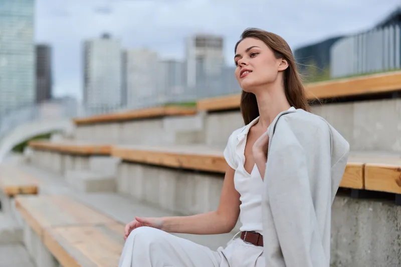 Stylish woman in business attire exuding confidence against a modern urban backdrop with a soft color palette, showcasing professionalism and elegance.