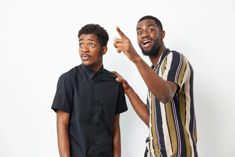 Two African American men interacting joyfully, one pointing while the other looks surprised, showcasing a moment of excitement. Perfect for celebratory themes.