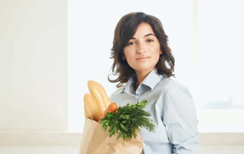 Брюнетка с пакетом продуктов: овощи, зелень, покупки в супермаркете