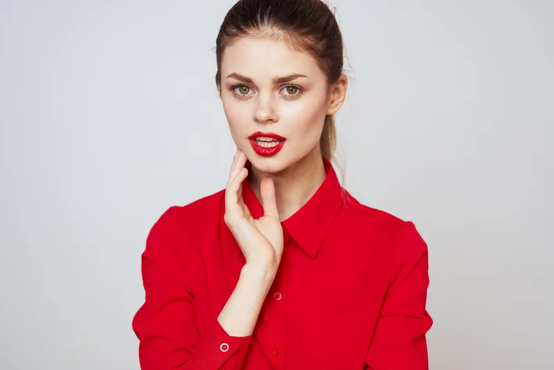Портрет женщины с красными губами в рубашке на светлом фоне, обрезанный вид, модельный макияж и причёска