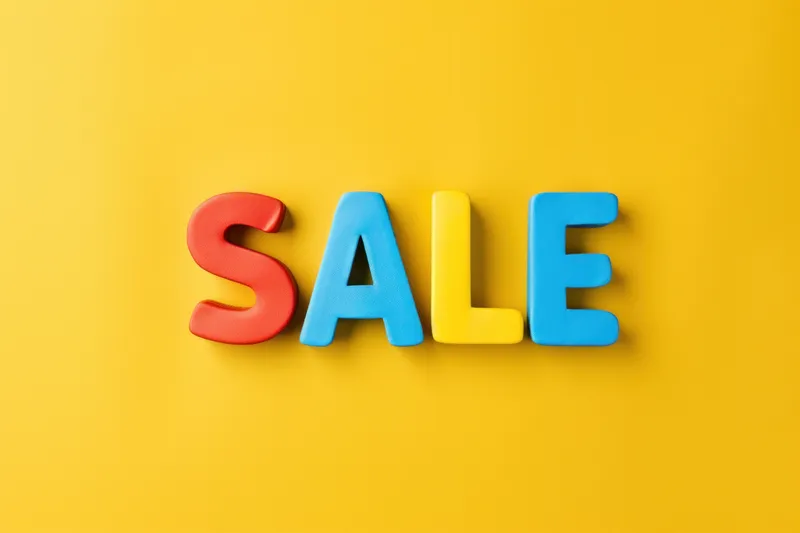 На желтом фоне разноцветные пластиковые буквы sale