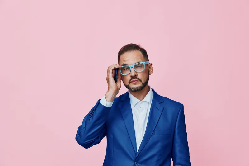A professional man in a blue suit stands against a solid pink background, conveying business focus, confidence, and calm emotion for corporate, marketing, and entrepreneurial needs.