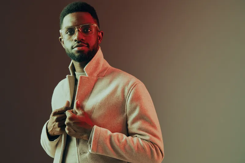 Stylish young man with glasses in a beige jacket against a warm gradient background, exuding confidence and elegance, perfect for fashion and lifestyle concepts