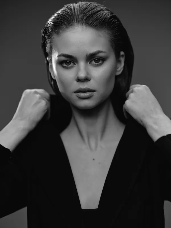 Black and white portrait of a confident woman with intense gaze wearing a dark blazer in dramatic lighting.