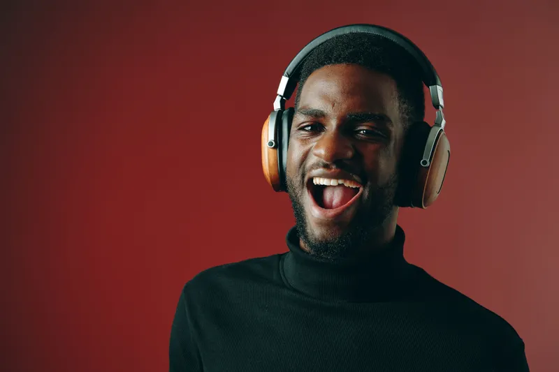 Happy young black man enjoying music with headphones on a vibrant red background, showcasing joy and energy in a stylish outfit