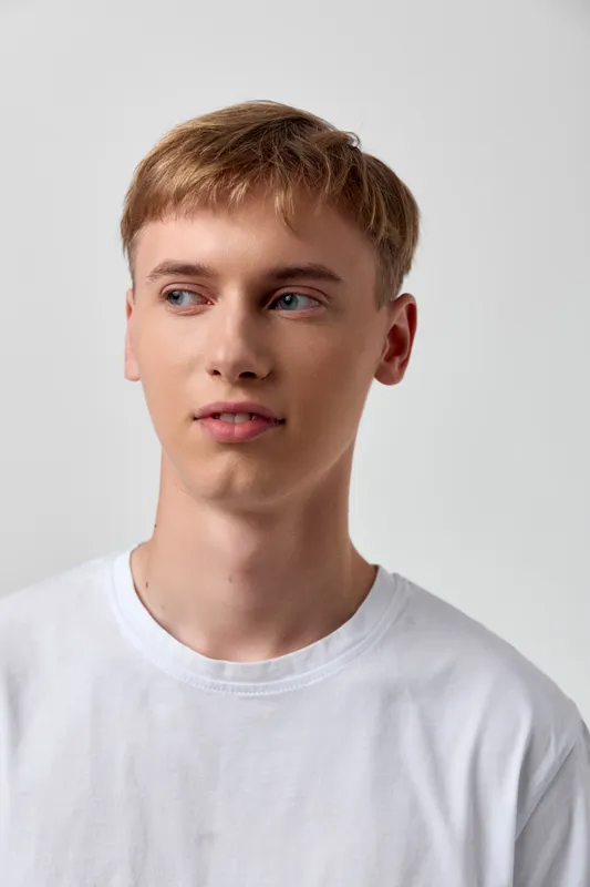 Man in a white t shirt looking to the side, clean studio backdrop, casual fashion style, confident pose, simple composition, neutral lighting, everyday wear for lifestyle and fashion stock imagery