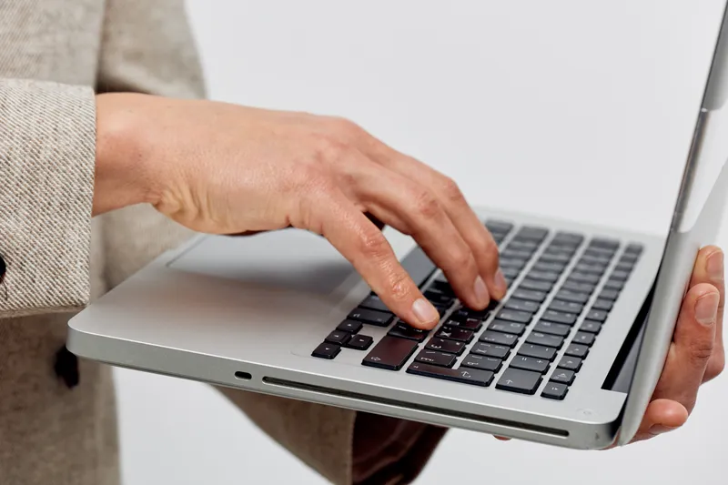 Woman using a silver laptop in hand, close-up view, workspace scene, modern technology, professional setting, casual workplace atmosphere, with a focus on digital device.