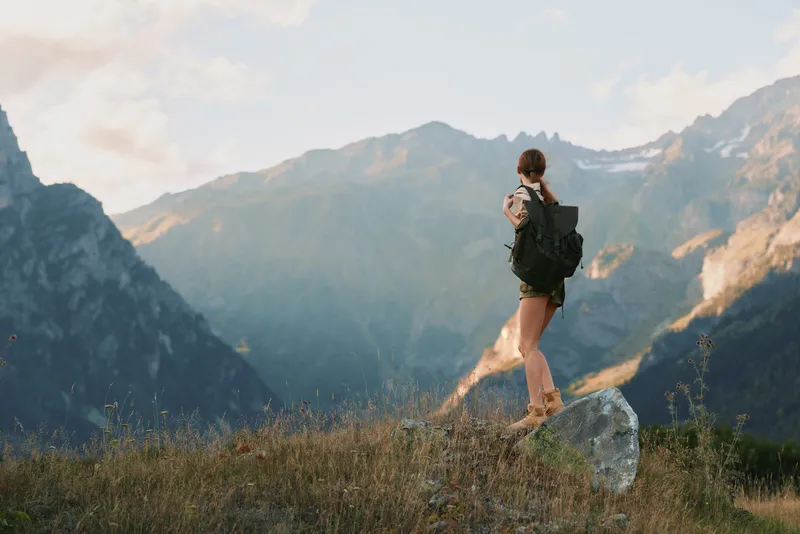 Woman hiking with a backpack in a rugged mountain landscape, embracing outdoor nature and adventure during travel. A bright, scenic moment on a wide alpine meadow.