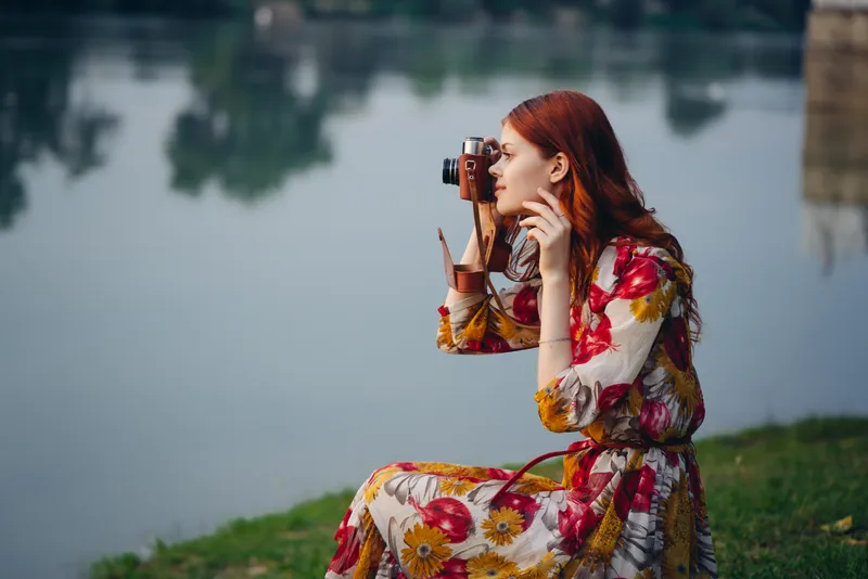 Женщина в платье с фотоаппаратом на природе, фотографирует реку, хобби