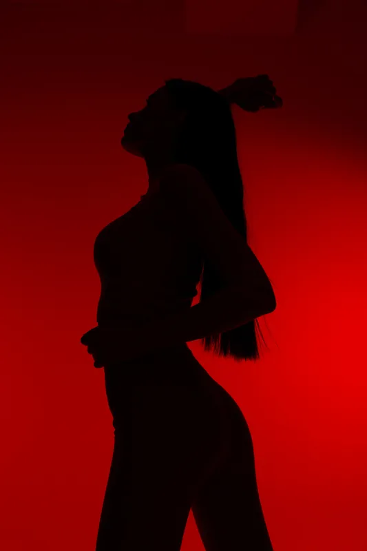 Silhouette of a woman sport fitness performing exercise with defined curves against vibrant red background, emphasizing strength, health, and active lifestyle.